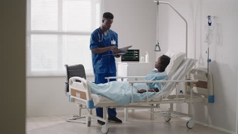 Afroamerikanische-Frau-Ruht-Nach-Der-Operation-Im-Krankenhausbett-Und-Spricht-Mit-Einem-Jungen-Krankenpfleger.-Porträt-Einer-Afroamerikanischen-Krankenschwester,-Die-Einer-Kranken-Patientin-Im-Bett-Hilft
